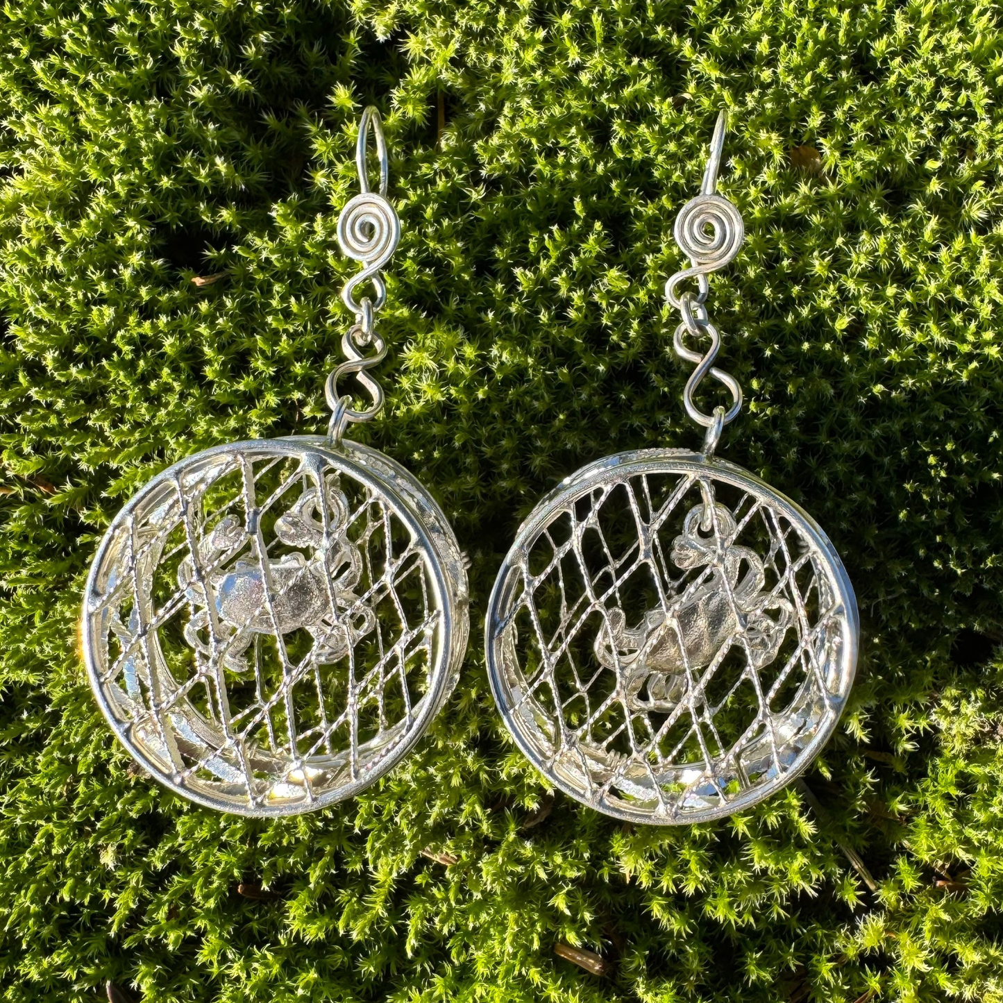Silver circular earrings with intricate designs on a green moss background